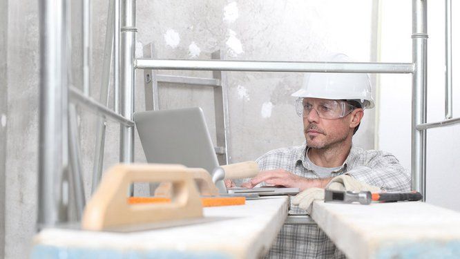 photo d'un homme avec casque de chantier travaillant sur une ordinateur avec texte : #COVID-19