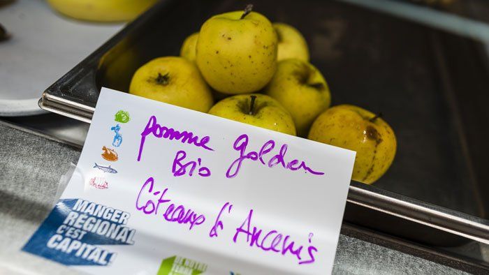 Gros plan sur des pommes Golden dans un restaurant scolaire avec une étiquette "Manger Local c'est capital"