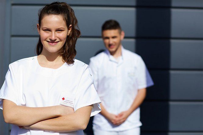 1 jeune femme souriante en blouse blanche, derrière elle un jeune homme en blouse blanche également,