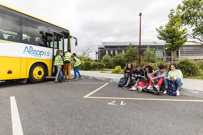 Car Aléop devant un établissement scolaire avec encadrant en gilets jaunes et un groupe d'élèves assis sur le trottoir