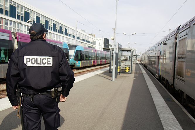 policier de dos sur le quai d'une gare, trains ter à quais