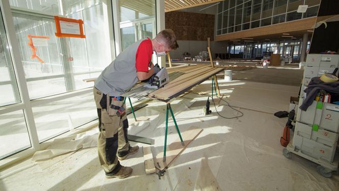 Jeune homme en train de scier une planche sur un chantier de bâtiment