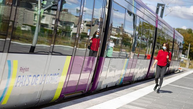 jeune femme masquée sur un quai de gare devant un TER