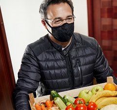 Homme avec  un masque qui livre à domicile des fruits et légumes à une personne âgée 