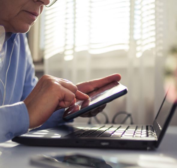 personne assise à un bureau tenant un smartphone dans le main devant un écran d'ordinateur portable